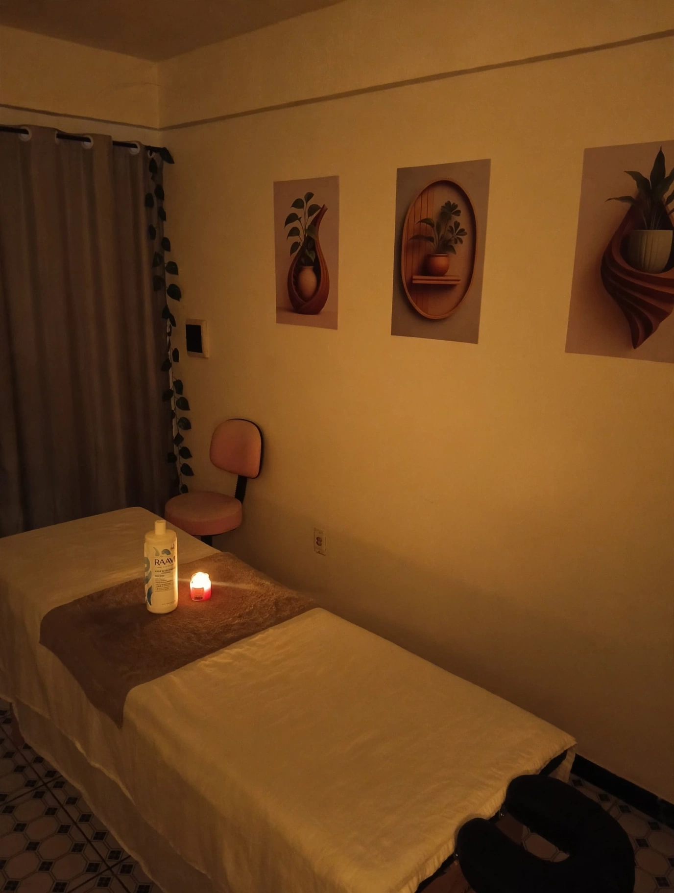 Sala de massagem com maca, óleo, vela acesa e quadros na parede