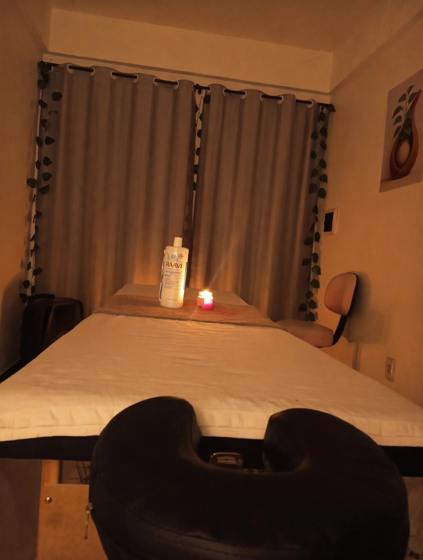 Maca de massagem vista de frente, com óleo, vela e banqueta ao fundo