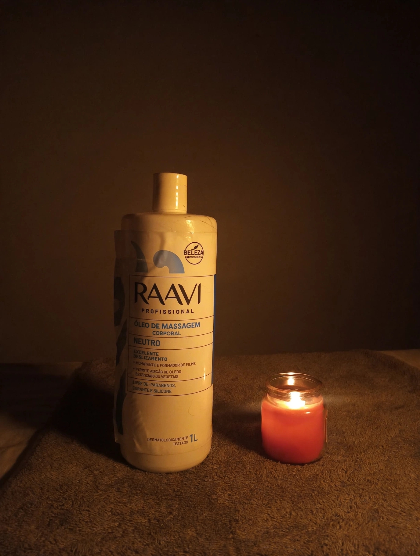 Frasco de óleo de massagem e vela acesa sobre a toalha