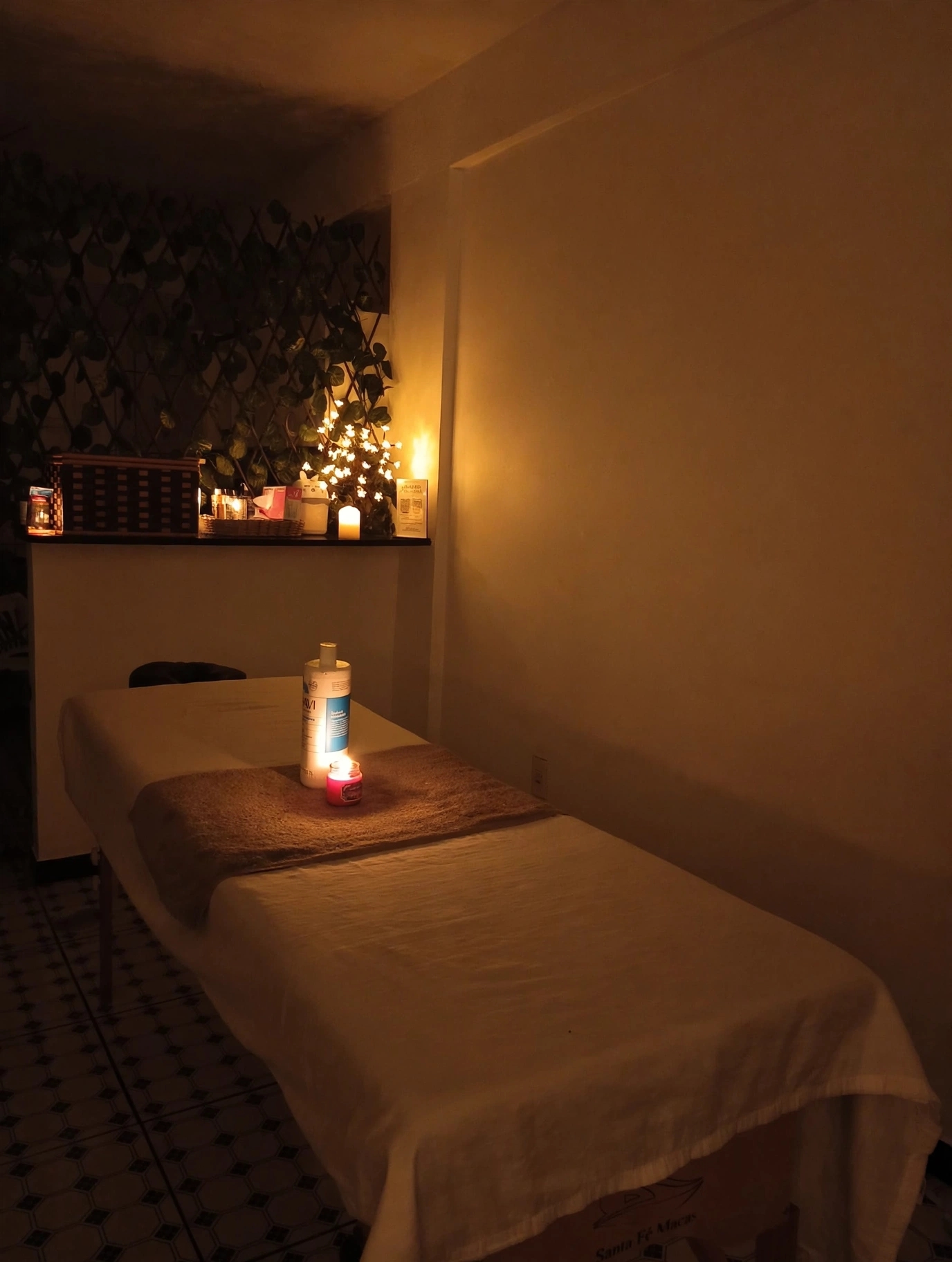 Maca de massagem iluminada por vela, com luzes e folhagens ao fundo